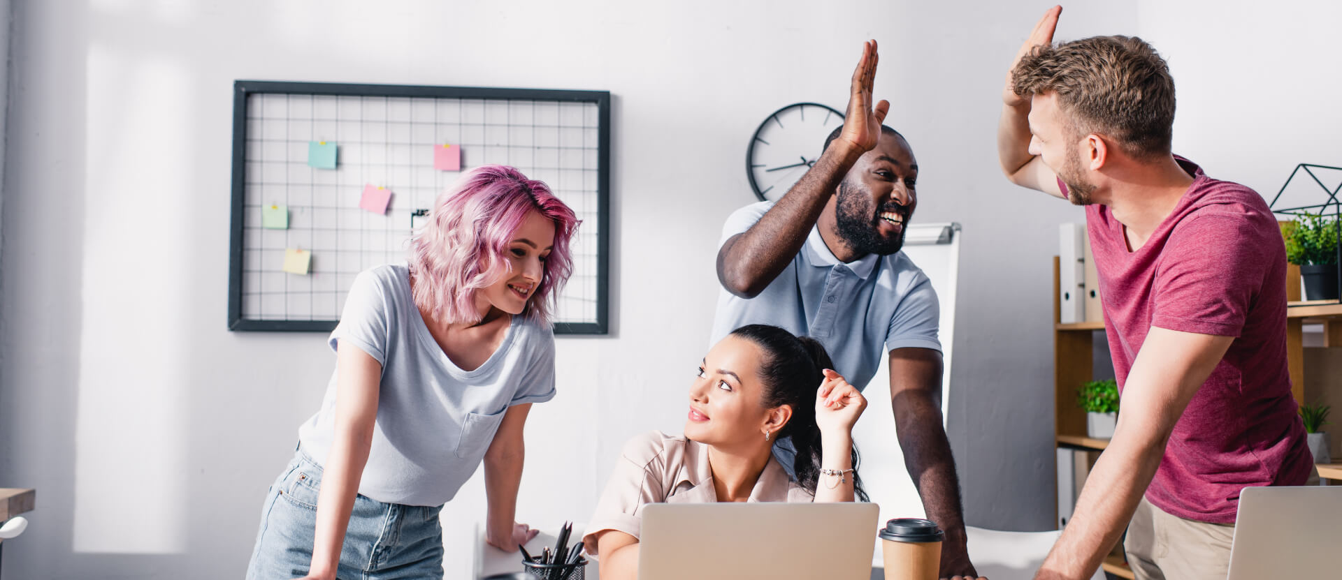 mixed group of men and women in an office area cheering and giving high fives<br />
