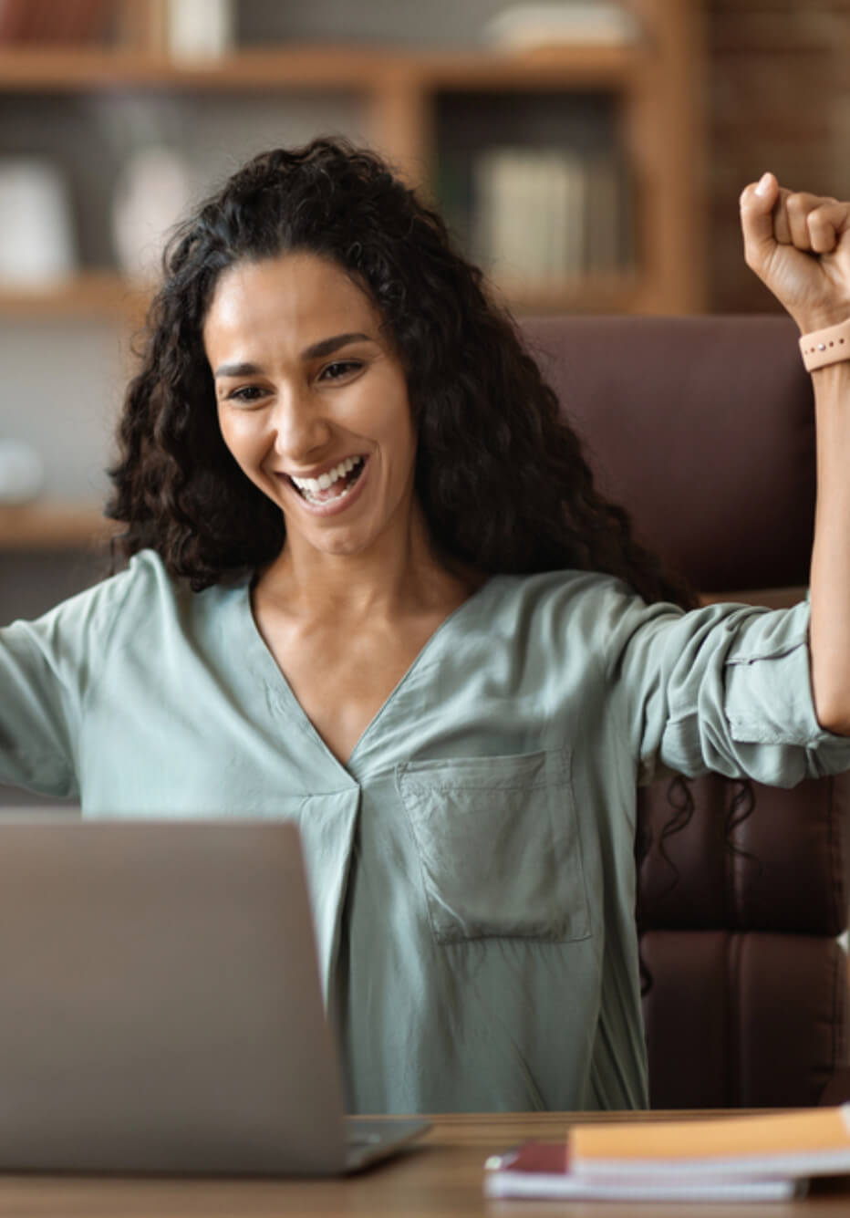 woman sitting in front of an open laptop cheering with her arm in the air